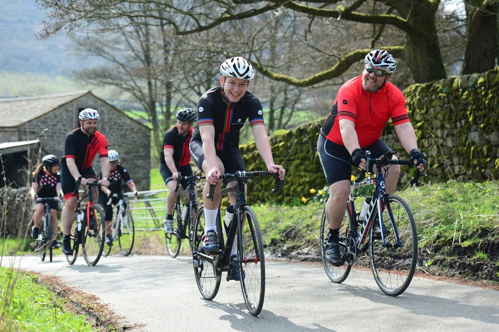 A group of cyclists riding up a country lane, smiling