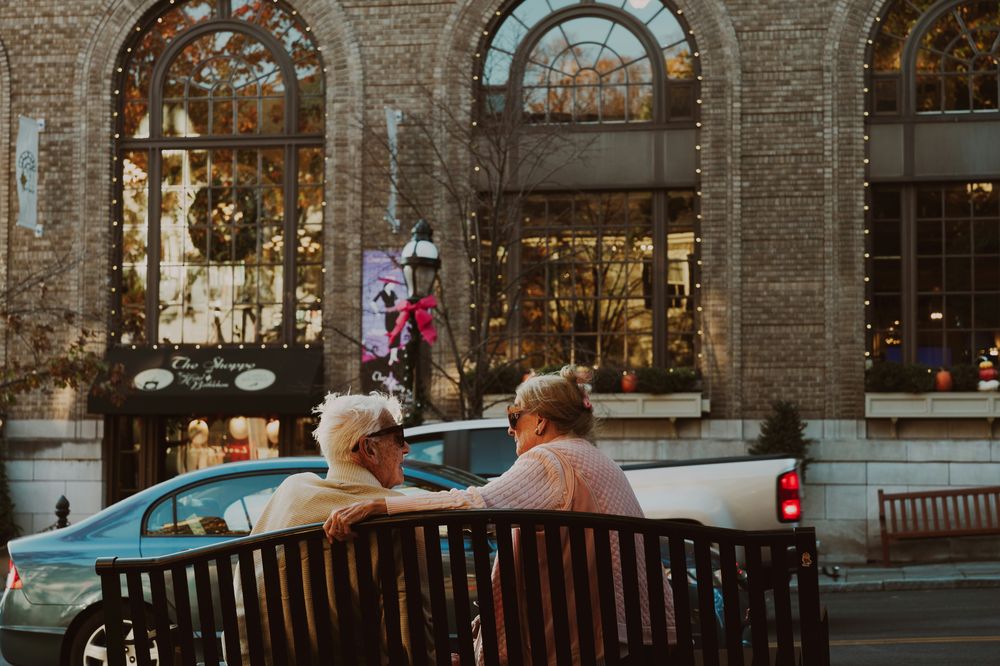 Two women chatting on a bench on a warmly lit evening street