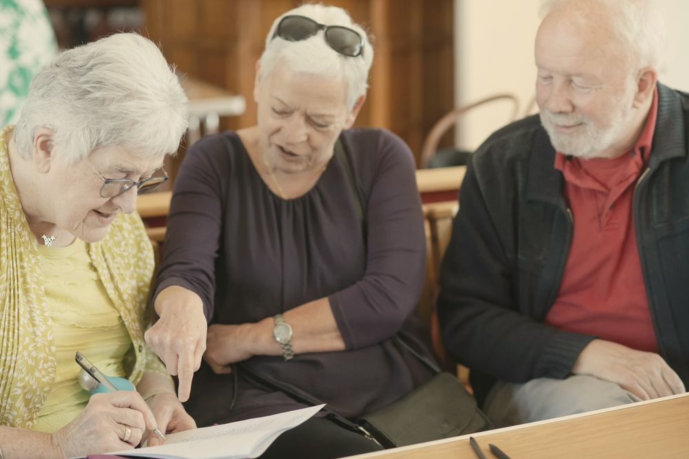 Three older people sitting together going through a document, one pointing at the page